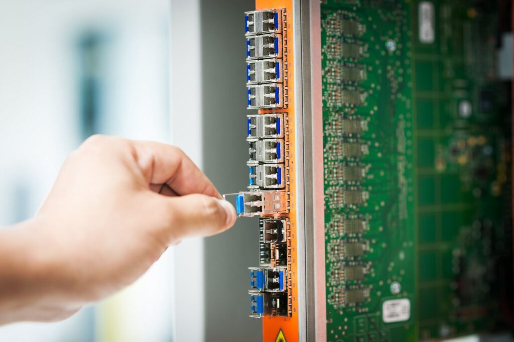 An individual connecting a cable into a network server port indoors, focusing on technology setup.